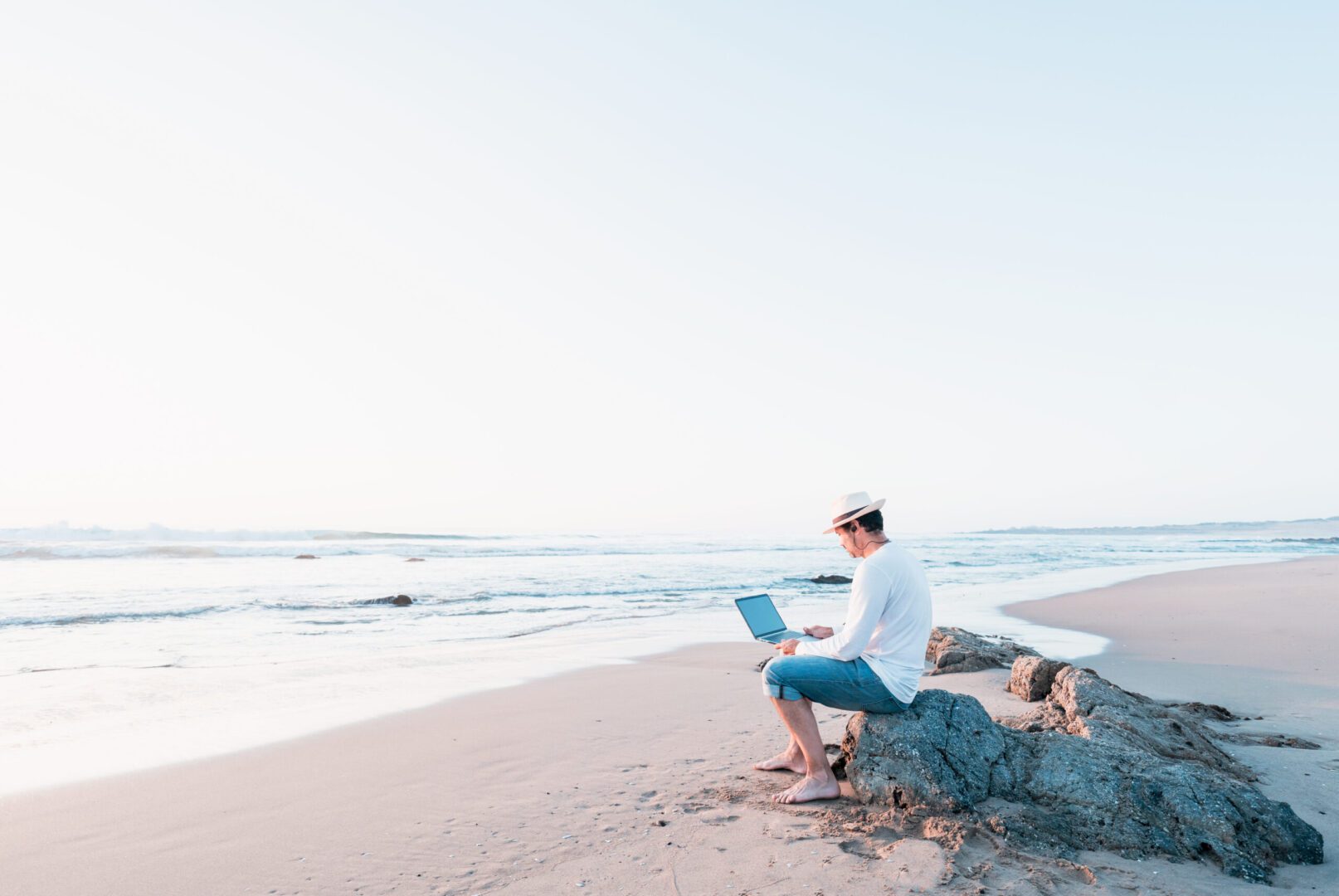 A man sitting on the beach with his laptop.