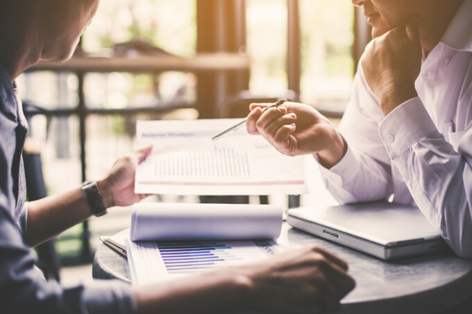 A woman is holding a pen and paper while talking to another person.